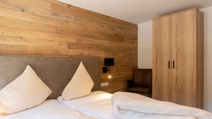 Une chambre d’hôtel avec une tête de lit en bois, deux lits avec du linge de lit blanc, une armoire en bois et un luminaire fixé au mur.