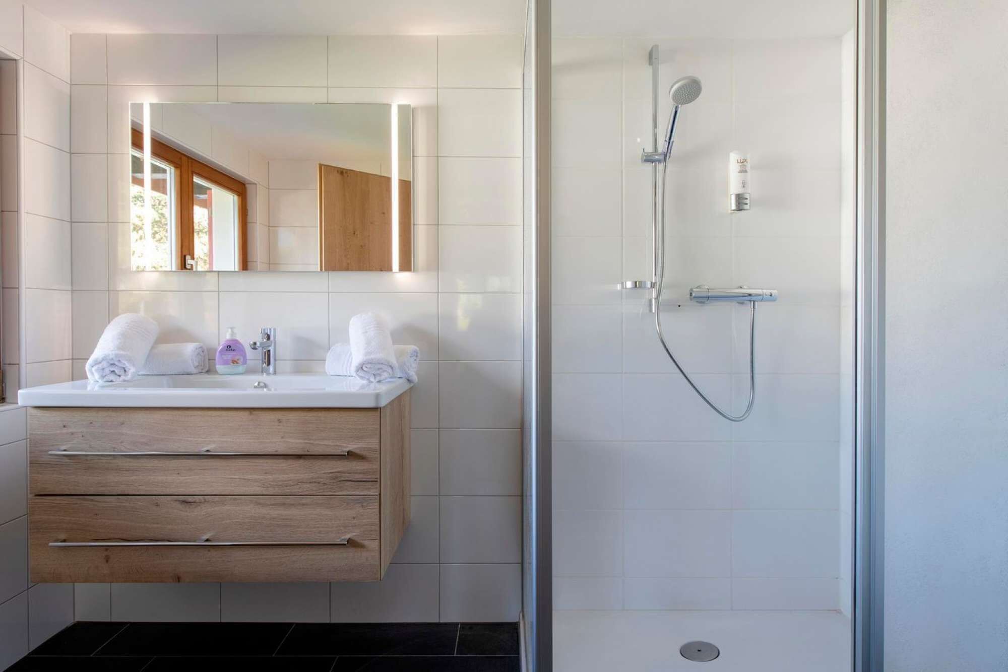 Ein modernes Badezimmer mit einem Holzwaschtisch, einem großen Spiegel und einer Duschkabine aus Glas.