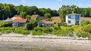 Un quartier résidentiel situé sur la côte, avec des maisons, une plage de sable et une vue dégagée sur la mer.