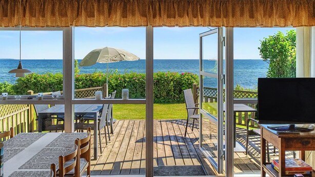 Un espace extérieur abrité, doté d’un plafond en bois, d’une table avec des chaises, d’un téléviseur et offrant une vue sur la mer.
