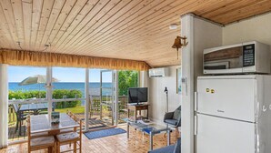 Une terrasse en bois avec une table et des chaises pour les repas, un canapé, un téléviseur, un réfrigérateur et une vue sur la mer.