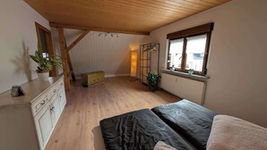 Ein Schlafzimmer mit Holzboden, einem Bett, einem Schminktisch, einem Heizkörper und einem Fenster mit Pflanzen.
