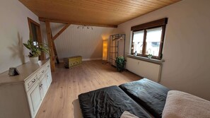 A bedroom with wooden flooring, a bed, a dresser, a radiator, and a window with plants. - Apartment by the forest in a quiet settlement panoramic window 5 min to the highway - center (Chemnitz)