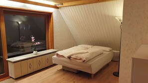 Een slaapkamer met een bed, een raam met een bloemenvaas en een houten kast.