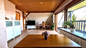 Ein Essbereich mit einem Holztisch, Stühlen, einem Fernseher und einem Blumentopf.