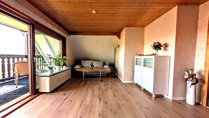 Ein gemütliches Zimmer mit Holzbalkendecke, einer Couch, einem kleinen Tisch und einer Vitrine.
