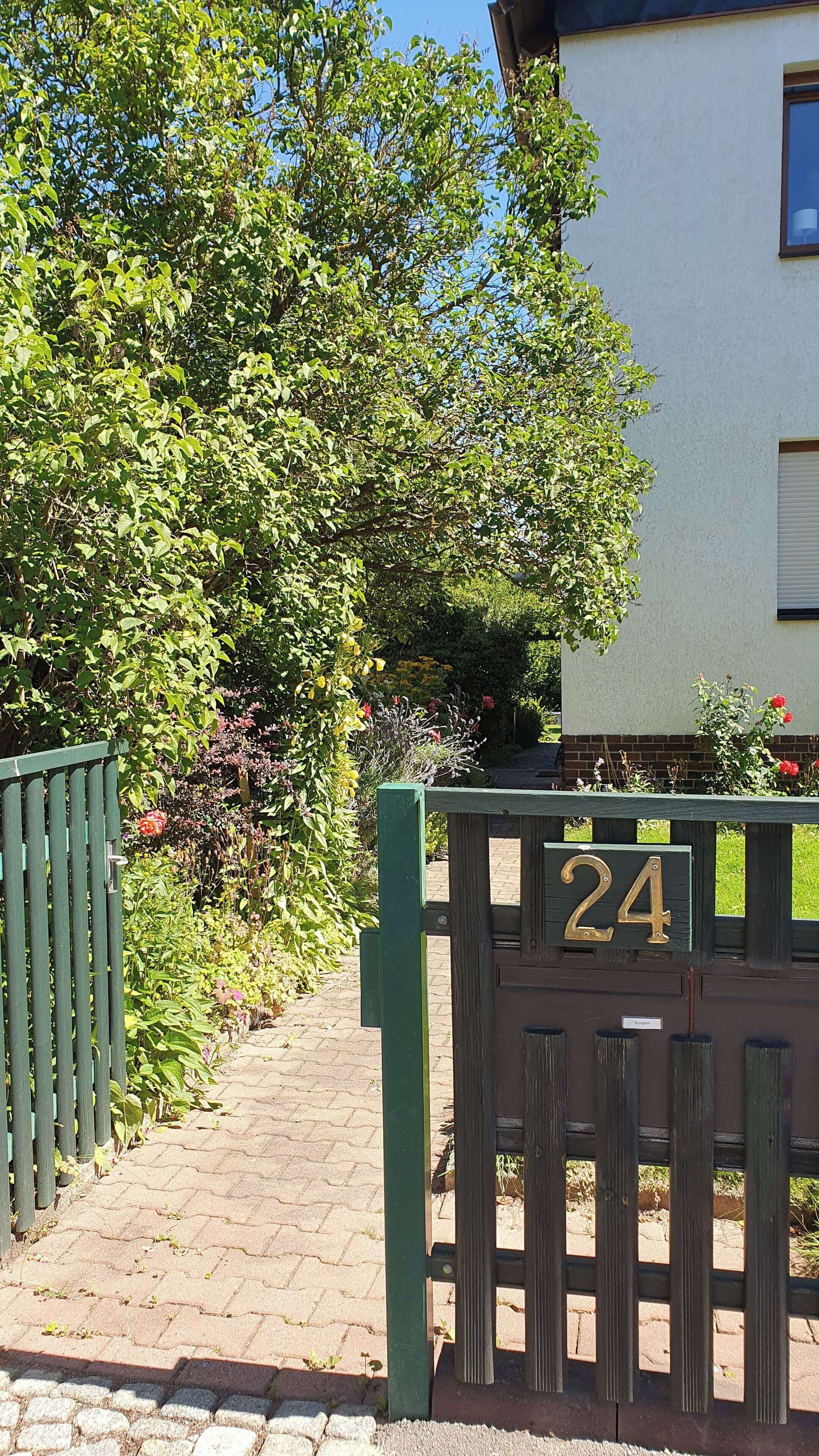 A gated entrance with a number sign, a paved pathway, and lush greenery.