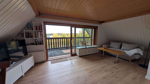 Ein gemütliches Zimmer mit Holzbalkendecke, einer Couch, einem Fernseher und einem Bücherregal.