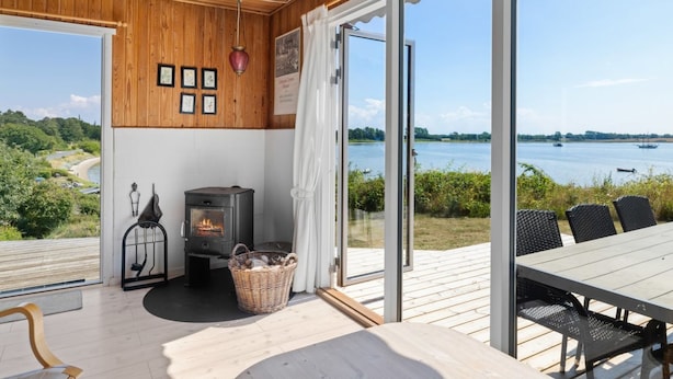 A cozy room with a wooden ceiling, a fireplace, and a large window overlooking a lake. - "Rajna" - 30m from the sea by Interhome (Martofte)