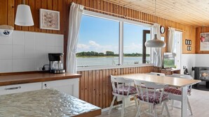 A kitchen with a large window, wooden walls, a stove, and a dining area with chairs. - "Rajna" - 30m from the sea by Interhome (Martofte)