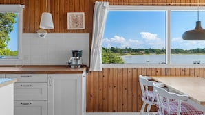 A kitchen with wooden walls, a white countertop, a coffee maker, and a view of a lake. - "Rajna" - 30m from the sea by Interhome (Martofte)