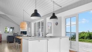Moderni keittiö, jossa on suuri keittiösaareke, valkoiset kaapit ja näkymä merelle.