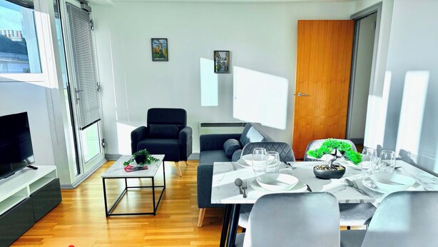 A modern living room with a sofa, a dining table set for two, a TV on a stand, and a small plant on a coffee table. - Bright 2-bed Apartment York City Centre - Walk to Everything (York)