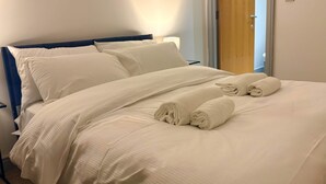 A neatly made bed with white linens and rolled towels, a wooden door to the right, and a white wall. - Bright 2-bed Apartment York City Centre - Walk to Everything (York)