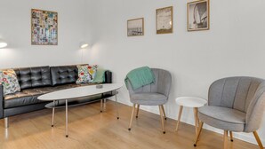A modern living room with a leather sofa, a round coffee table, and two grey armchairs. There are three framed artworks on the wall. - "Babo" - 250m from the sea by Interhome (Bogense)
