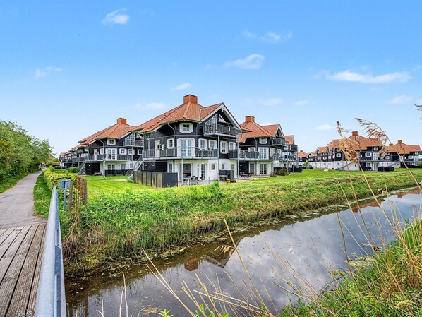 A row of traditional European-style houses with red-tiled roofs, a wooden boardwalk, and a canal.