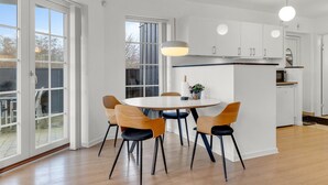 A modern kitchen with white cabinets, a central island, and a dining area with wooden chairs and a round table. - "Babo" - 250m from the sea by Interhome (Bogense)