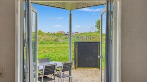 A patio area with a table and chairs, a covered seating area, and a view of a grassy field and buildings in the distance. - "Babo" - 250m from the sea by Interhome (Bogense)