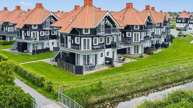 A row of modern, multi-story houses with red-tiled roofs, a grassy area, and a small water body. - "Babo" - 250m from the sea by Interhome (Bogense)