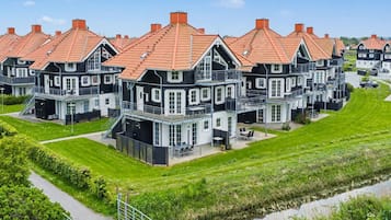 Une rangée de maisons modernes à plusieurs étages, avec des toits recouverts de tuiles rouges, une pelouse et un petit plan d’eau.