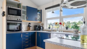 Una cocina moderna con armarios azules, horno integrado, microondas y un amplio ventanal con vistas a la vegetación.