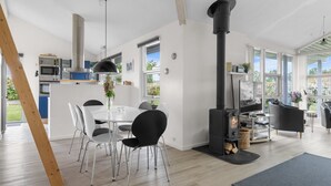 Una cocina moderna con electrodomésticos integrados, un comedor con mesa blanca y sillas negras, y una estufa de leña.
