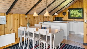 A modern kitchen with a wooden interior, a dining area with white chairs, and a large window providing natural light. - "Allin" - 350m from the sea by Interhome (Otterup)