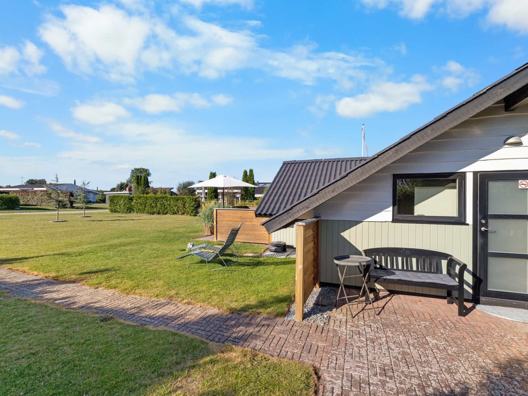 Une maison moderne dotée d’un patio, d’une terrasse en bois et d’un petit espace extérieur aménagé avec une table et des chaises.