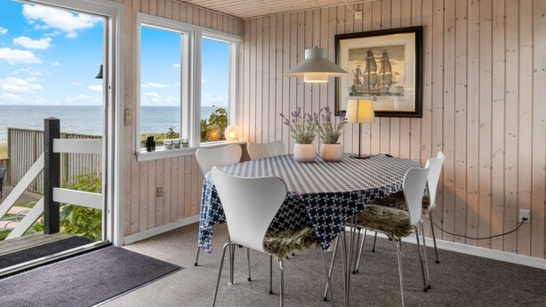 A dining area with a table set for four, a view of the sea through large windows, and a framed picture on the wall. - "Nedelko" - 20m from the sea by Interhome (Otterup)