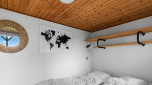 A bedroom with a wooden ceiling, a world map on the wall, a round mirror, and a bed with a patterned duvet. - "Nedelko" - 20m from the sea by Interhome (Otterup)