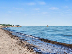 Una playa con arena, agua tranquila y un barco a lo lejos.