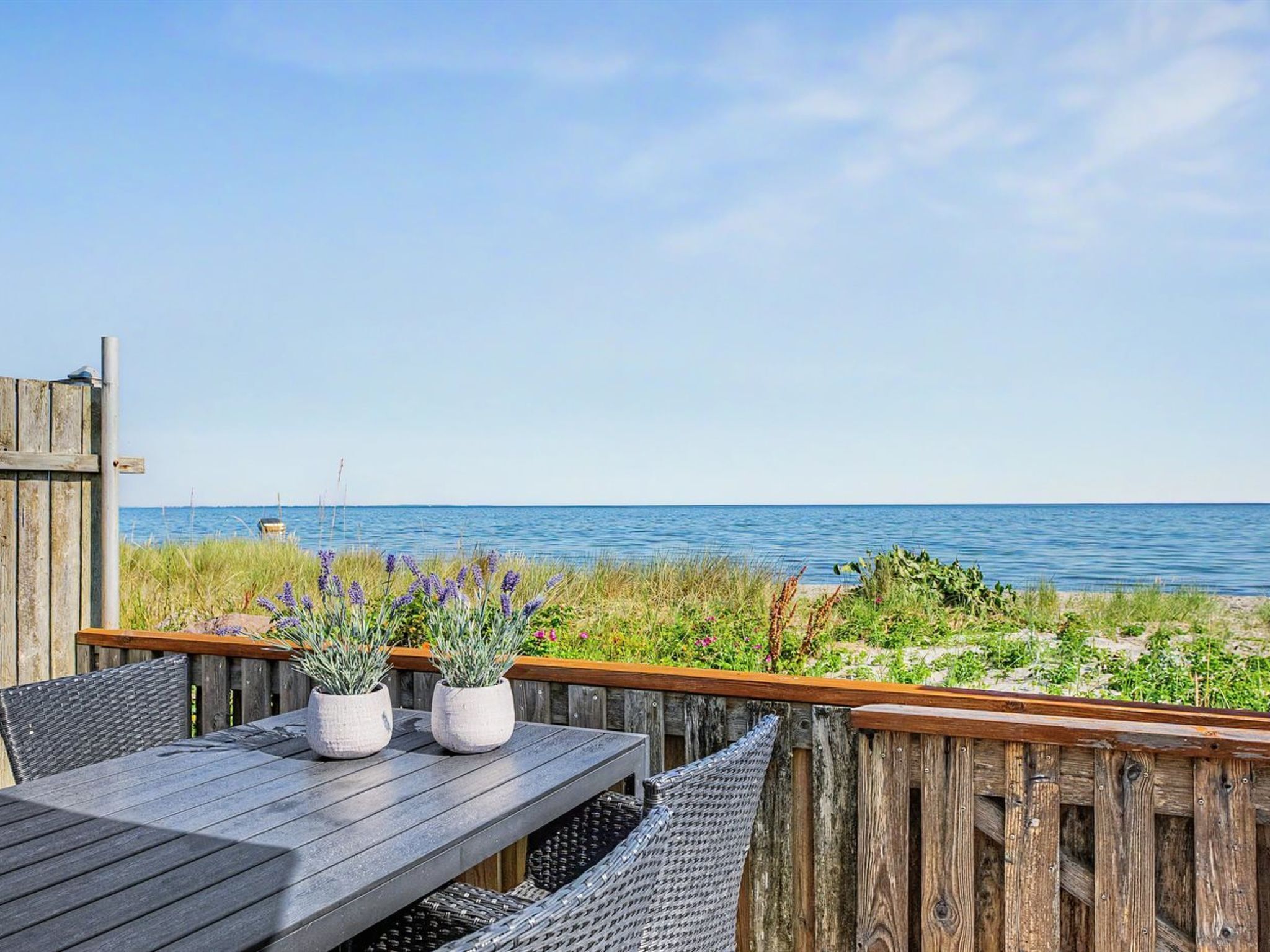 Une terrasse en bois avec une table et des chaises, donnant sur une étendue d’eau.