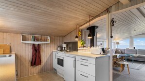 A modern kitchen with white cabinets, a built-in oven, and a coffee machine. There is a wooden ceiling and a view of the ocean through large windows. - "Nedelko" - 20m from the sea by Interhome (Otterup)