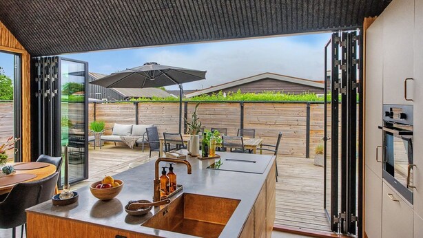 Een moderne keuken met een groot eiland, een eethoek met tafel en stoelen, en uitzicht op de achtertuin.