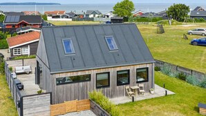 Een modern huis met een schuin dak, grote ramen en een terras met tuinmeubilair.