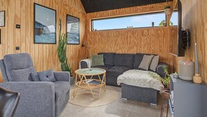 Een gezellige kamer met een grijze bank, een ronde rieten salontafel en een groot raam met uitzicht.