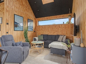 Ein gemütliches Zimmer mit einem grauen Sofa, einem runden Korbtisch und einem großen Fenster mit Blick.