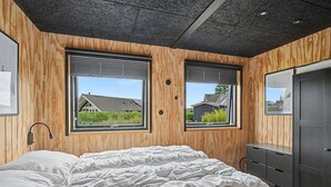 Een slaapkamer met een bed, houten wanden, twee ramen en een kledingkast.