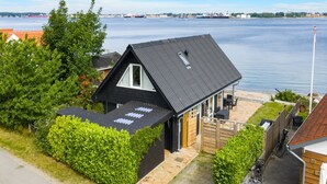 Ein modernes Haus mit Satteldach, einer kleinen Veranda und Blick auf ruhiges Wasser.