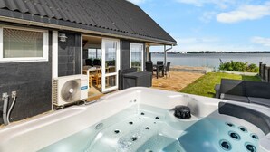 Ein modernes Haus mit Whirlpool, überdachter Terrasse und Blick auf das Wasser.