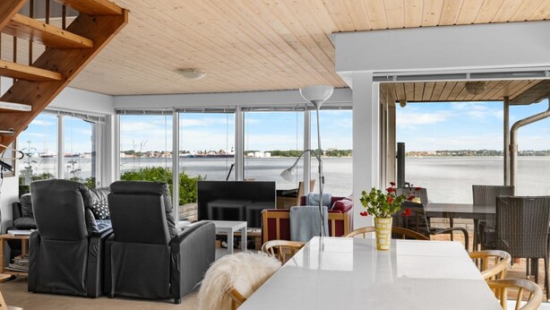 Ein modernes Interieur mit einem weißen Tisch, schwarzen Ledersesseln und Blick auf ein Gewässer.