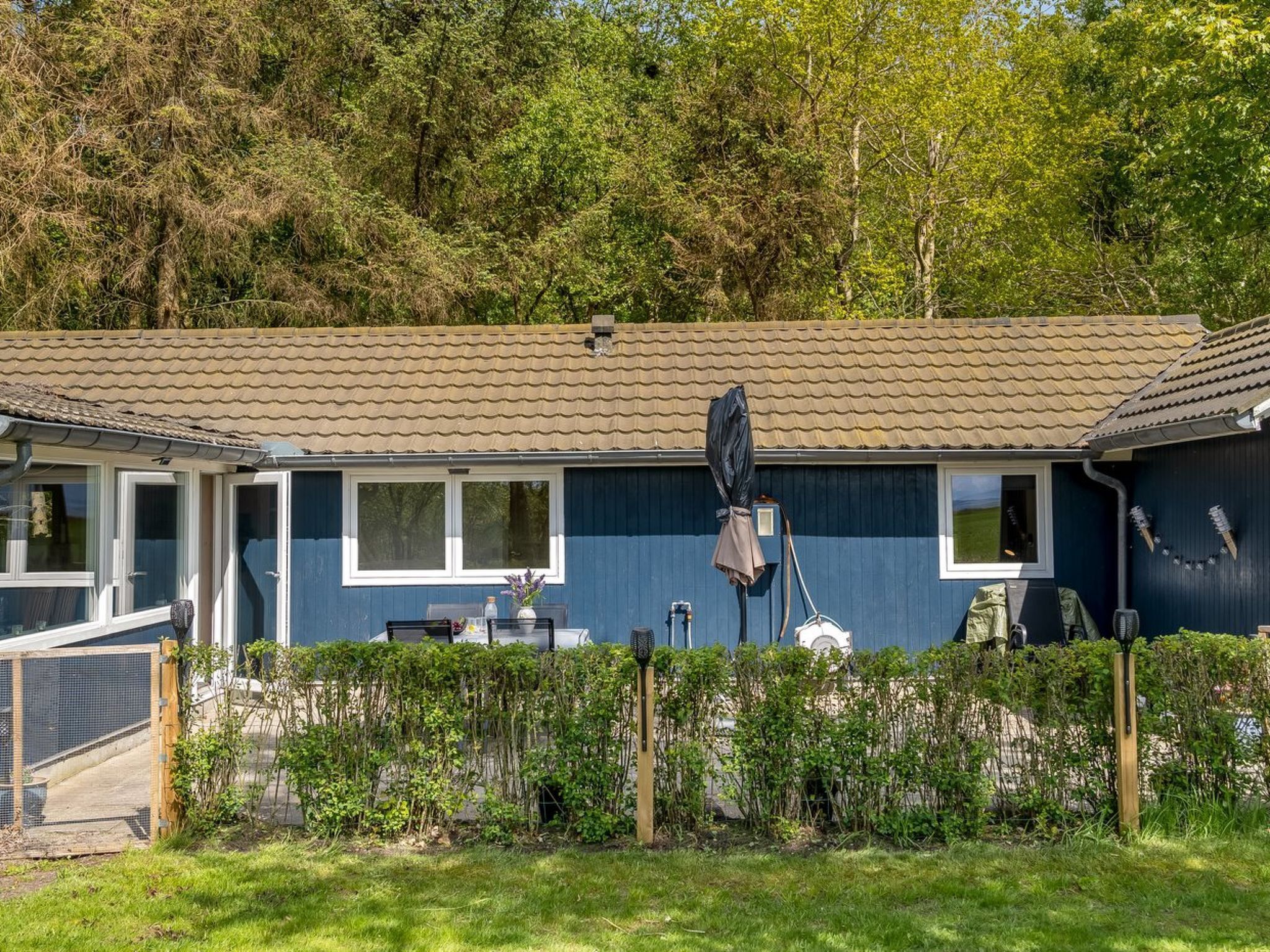 Een blauw gebouw met pannendak, een omheind erf en een tuin.