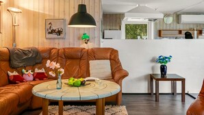 Una sala de estar acogedora con un sofá de cuero marrón, una mesita de centro redonda con un florero y una pequeña mesita auxiliar con un jarrón.