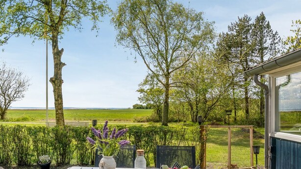 Un patio al aire libre con una mesa preparada para dos personas, rodeado de follaje y vistas a un campo.