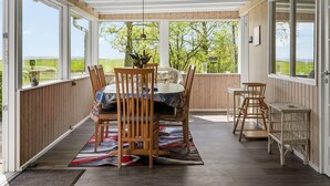 Un espacio cubierto para comer con mesa, sillas y vista a zonas verdes.