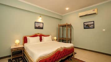 Habitación de hotel con una cama grande, una mesita de noche, una lámpara de noche, un aire acondicionado de pared y dos cuadros enmarcados.