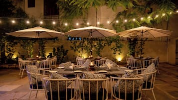 Un espacio al aire libre para comer con mesas, sillas, luces colgantes y sombrillas.