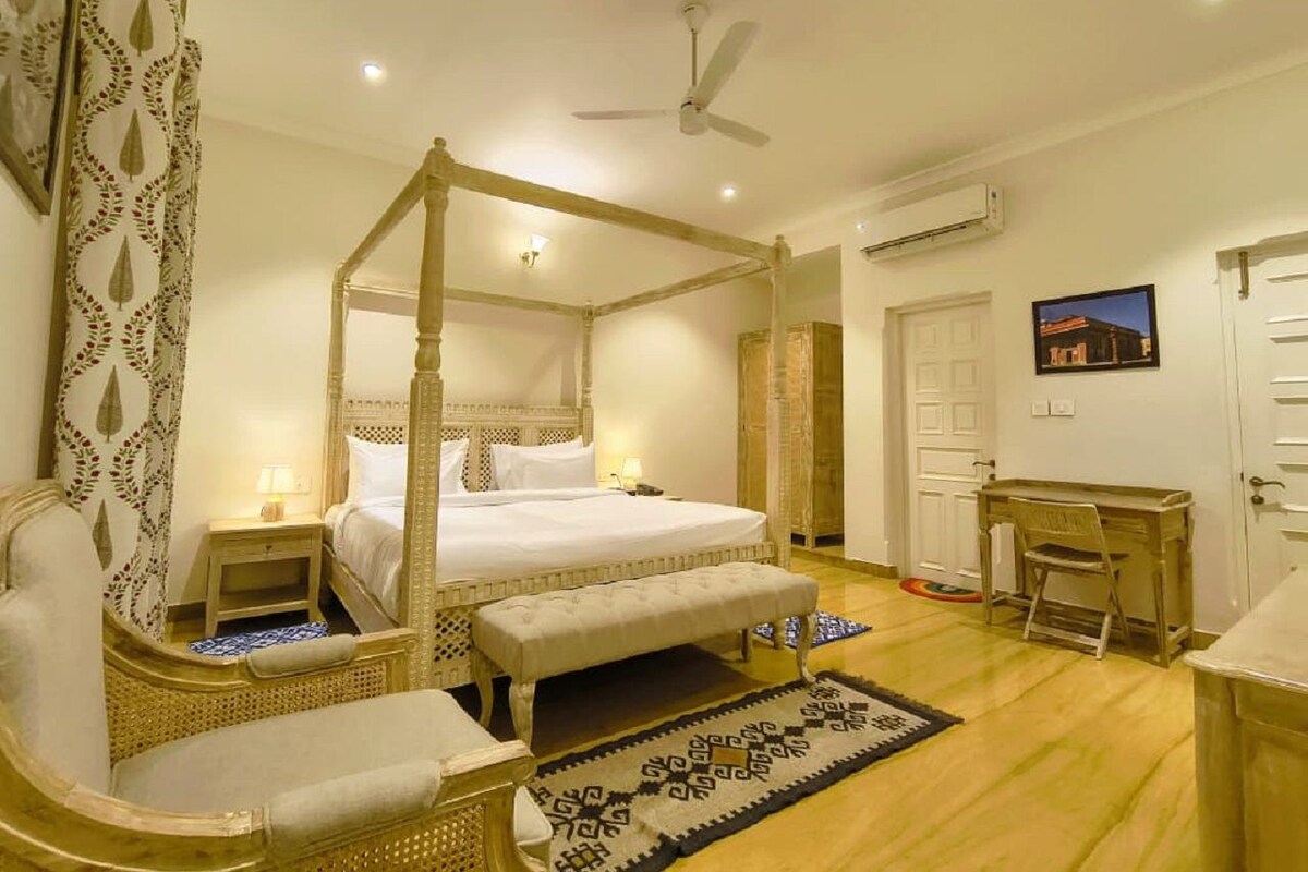 A four-poster bed with a canopy, a wooden desk, a chair, and a small bedside table with a lamp.