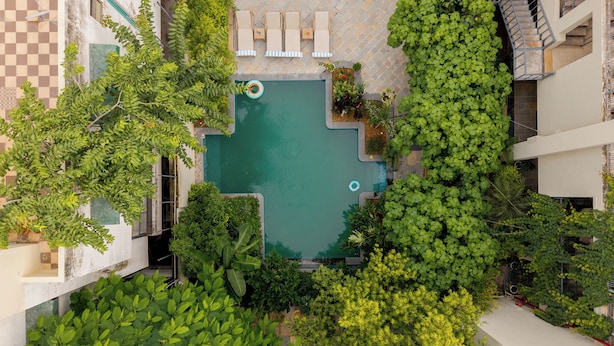 Vista aérea de una piscina en la azotea rodeada de abundante vegetación, con un piso de diseño a cuadros y mobiliario exterior.