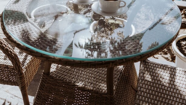 A glass table with two cups of coffee, surrounded by wicker chairs, overlooking a swimming pool with a building in the background. - Ramat Niwas by Kutani Stays (Jaipur)